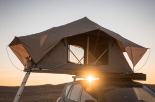 Ein Autodachzelt zum Campen auf dem Dachträger eines Geländewagens in der Wüste bei Sonnenuntergang